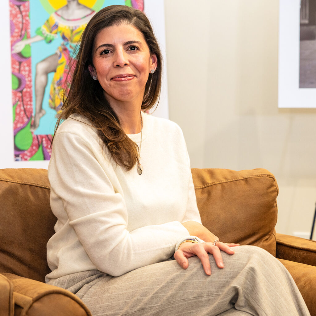 Moroccan woman smiling, sitting in a comfortable chair in front of artwork